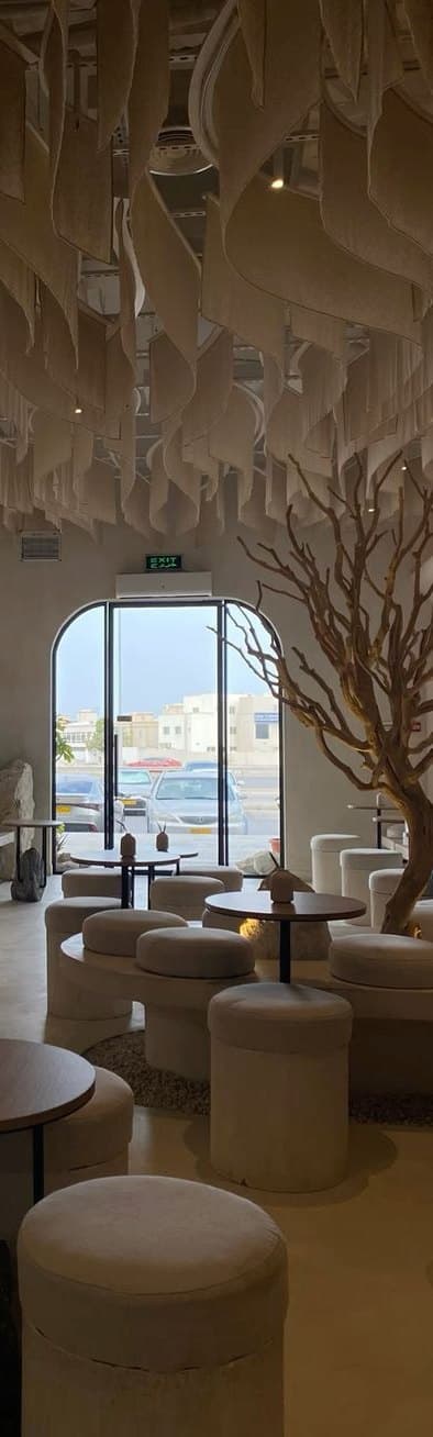 A café with round upholstered stools, small wooden tables, a sculptural bare tree and an arched glass door